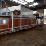 Horse stable walkway flooring with equestrian horsewoman holding a horse saddle.